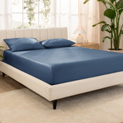 Organic cotton fitted sheet on a bed in a bedroom with a plant and window in the background