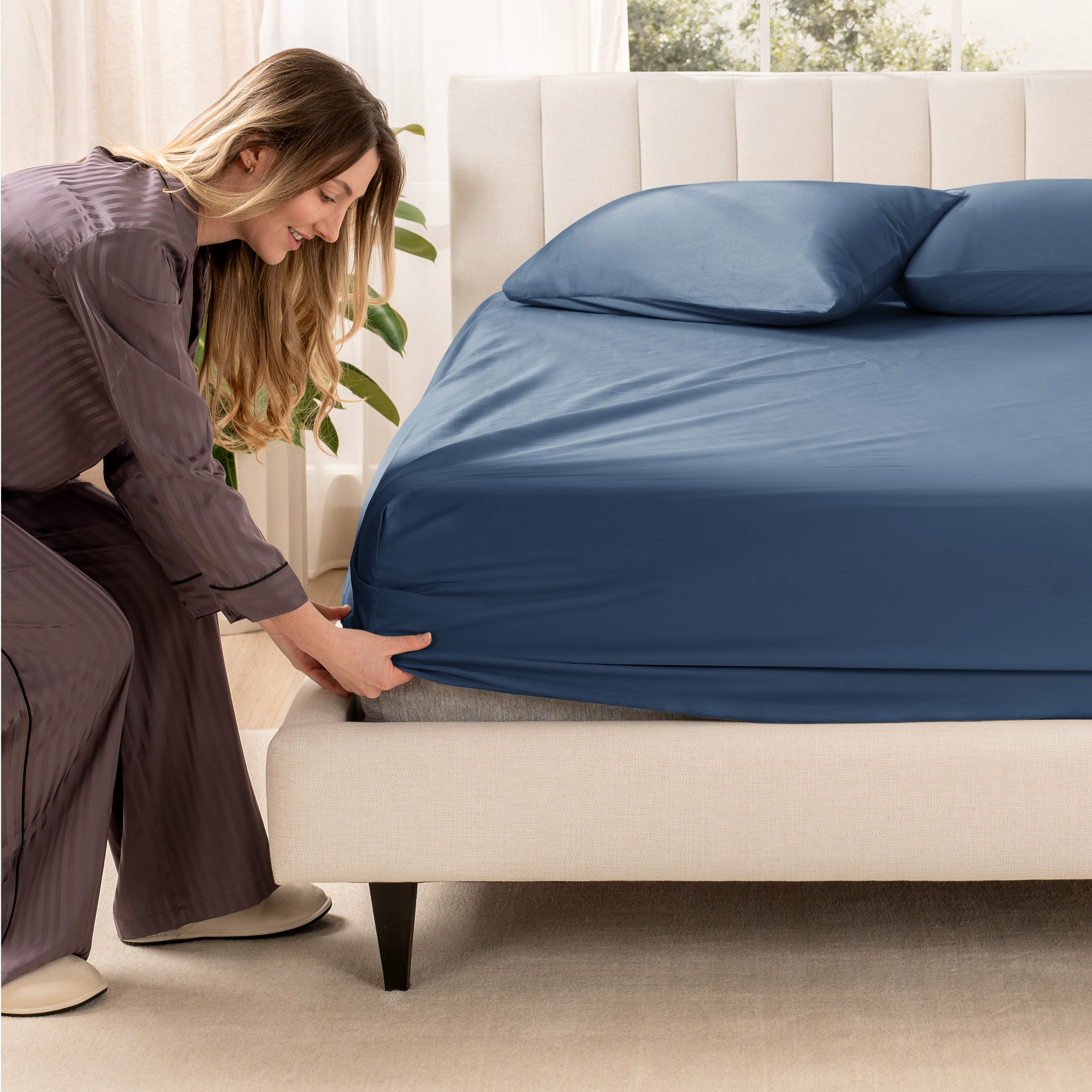 A woman is putting a fitted sheet on a mattress