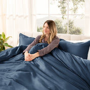 A woman sitting on a bed made with organic cotton sateen sheets and pillowcases