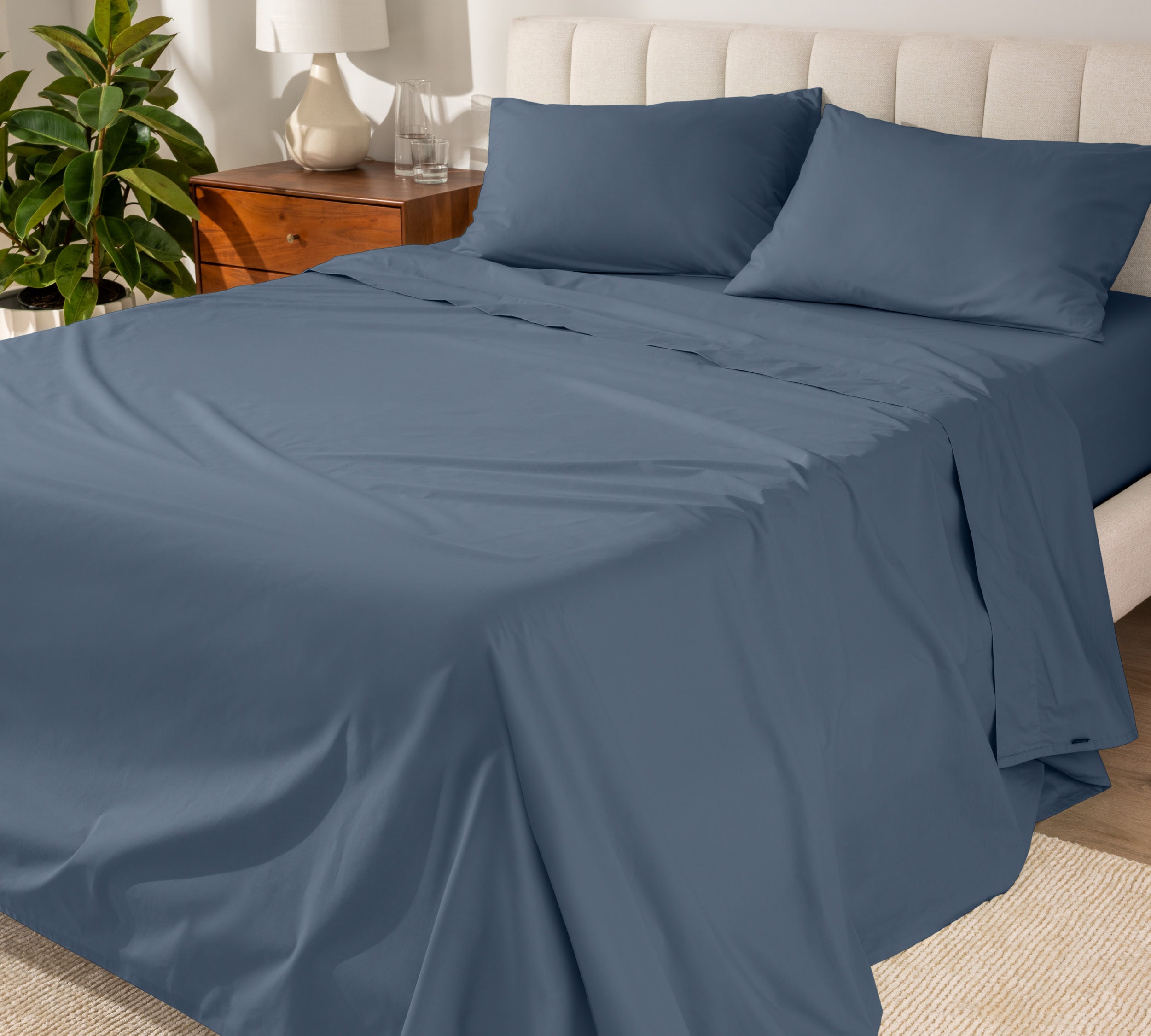 Organic cotton percale sheet set on a bed, with a flat sheet, fitted sheet, and two pillowcases displayed.