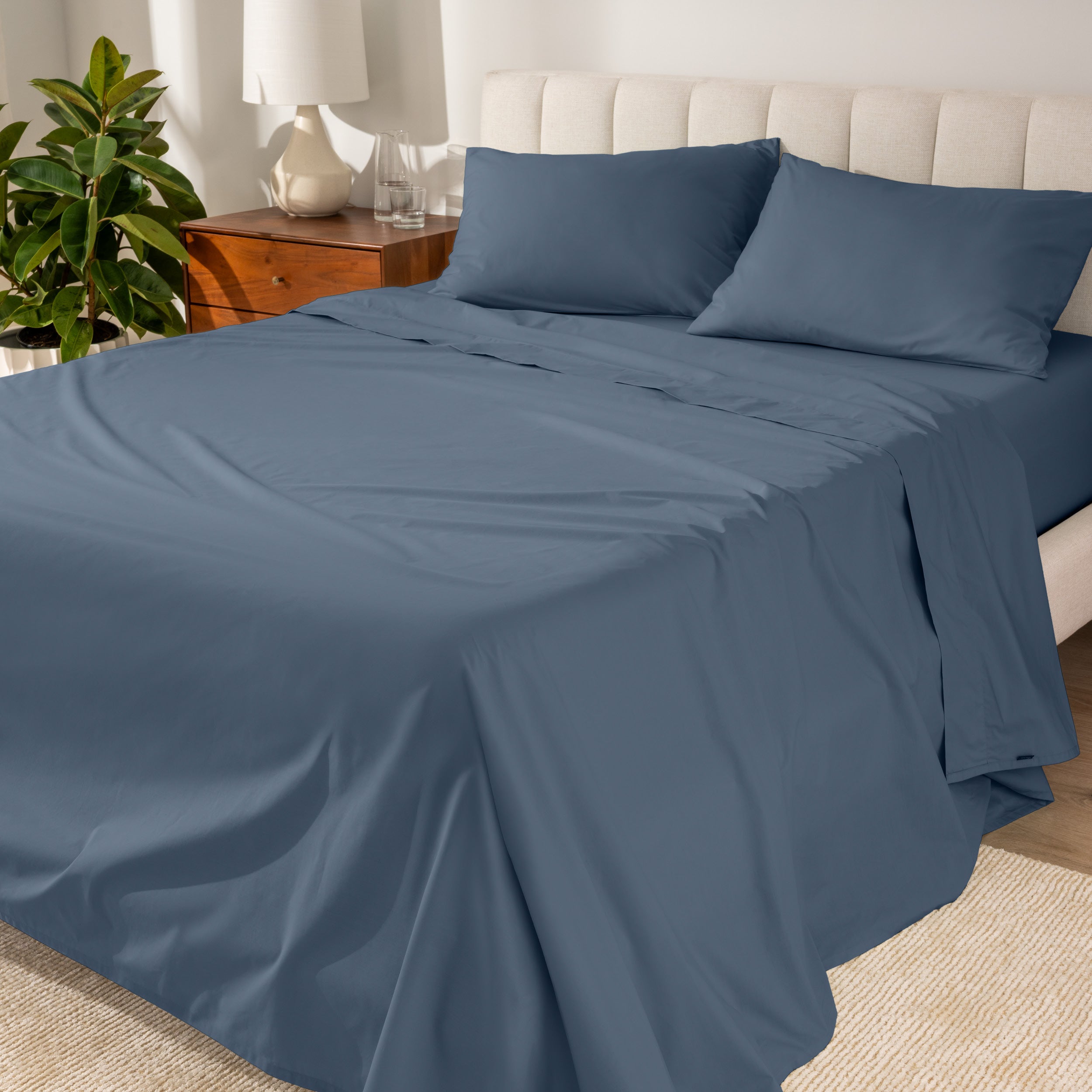 Organic cotton percale sheet set on a bed, with a flat sheet, fitted sheet, and two pillowcases displayed.