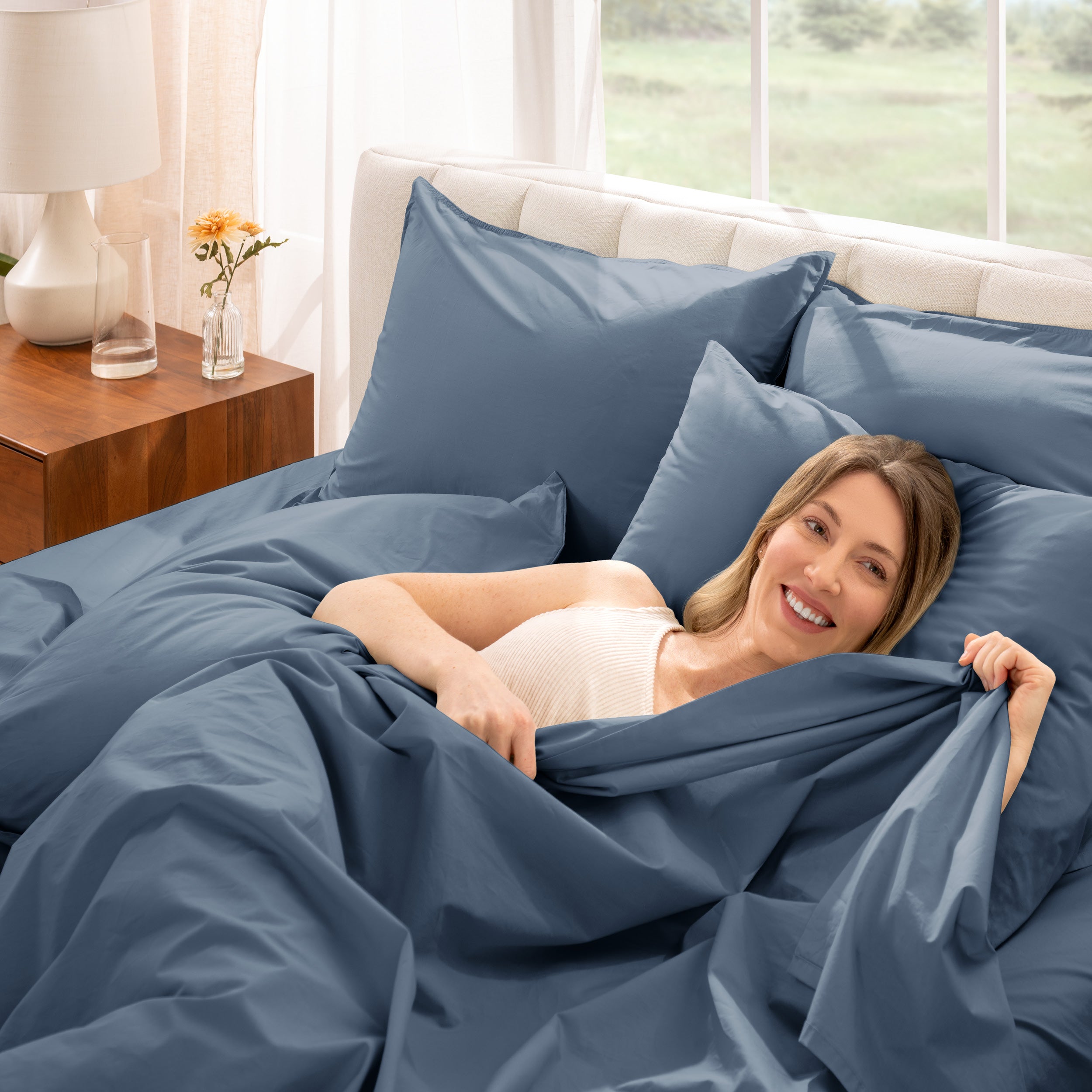 Woman lying in bed under percale sheets with a bright room setting