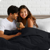 A couple sitting in bed with a comforter over them