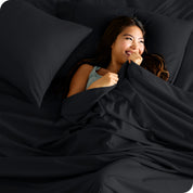A smiling woman on a bed with a microfiber sheet over her