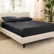Organic cotton fitted sheet on a bed in a bedroom with a plant and window in the background