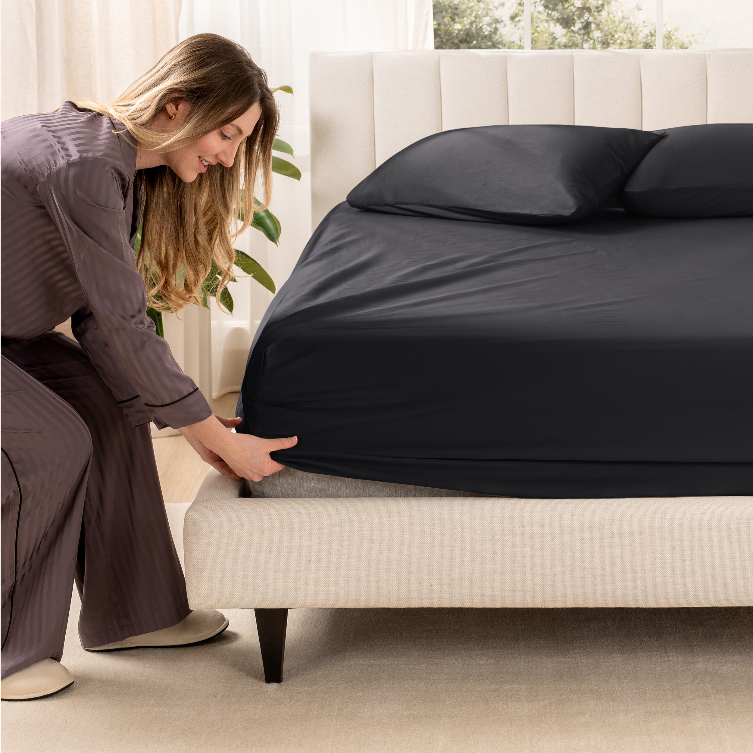 A woman is putting a fitted sheet on a mattress