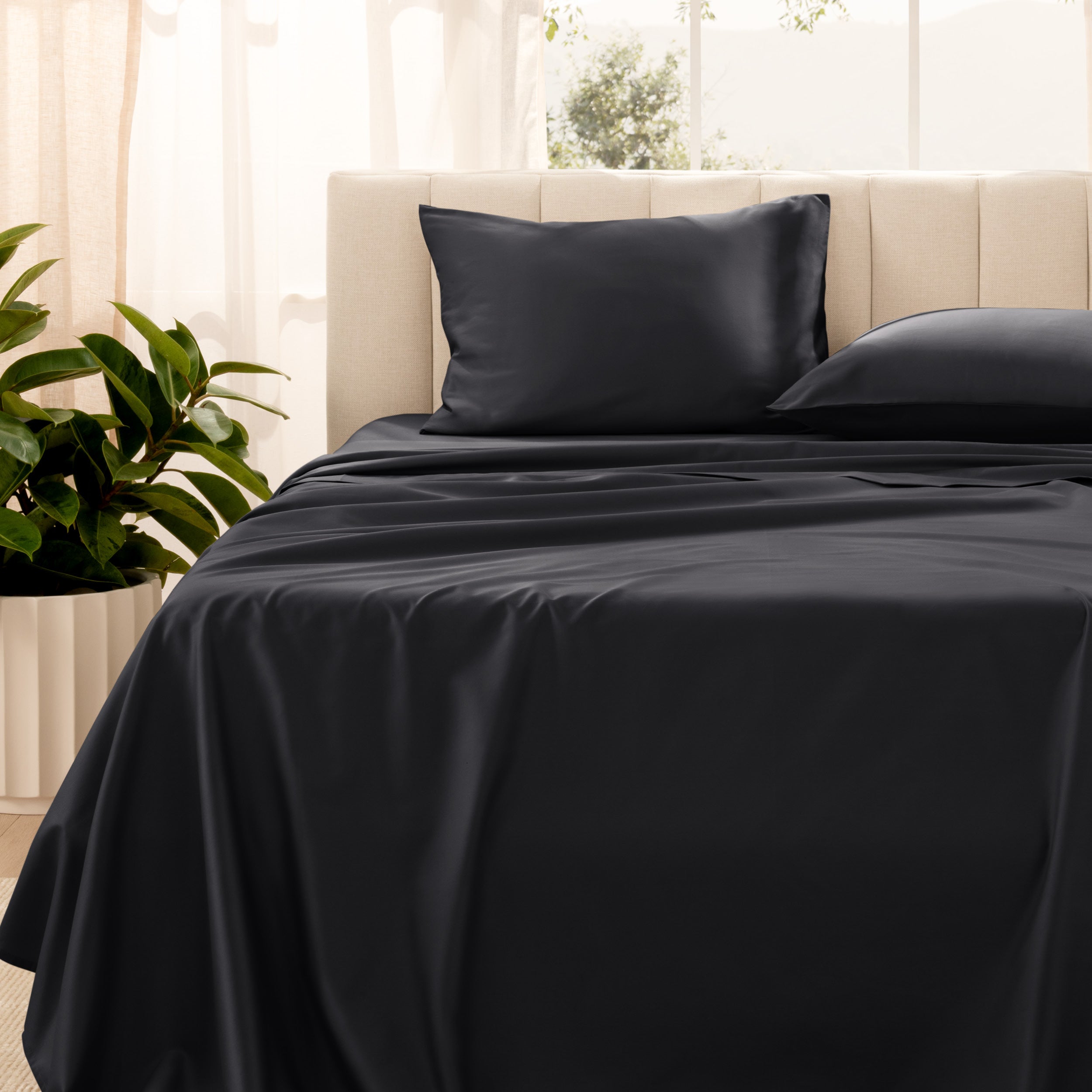 Organic sateen bedding on a bed with a beige headboard and plant in the corner.