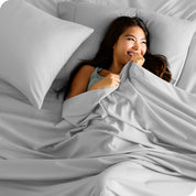 A smiling woman on a bed with a microfiber sheet over her