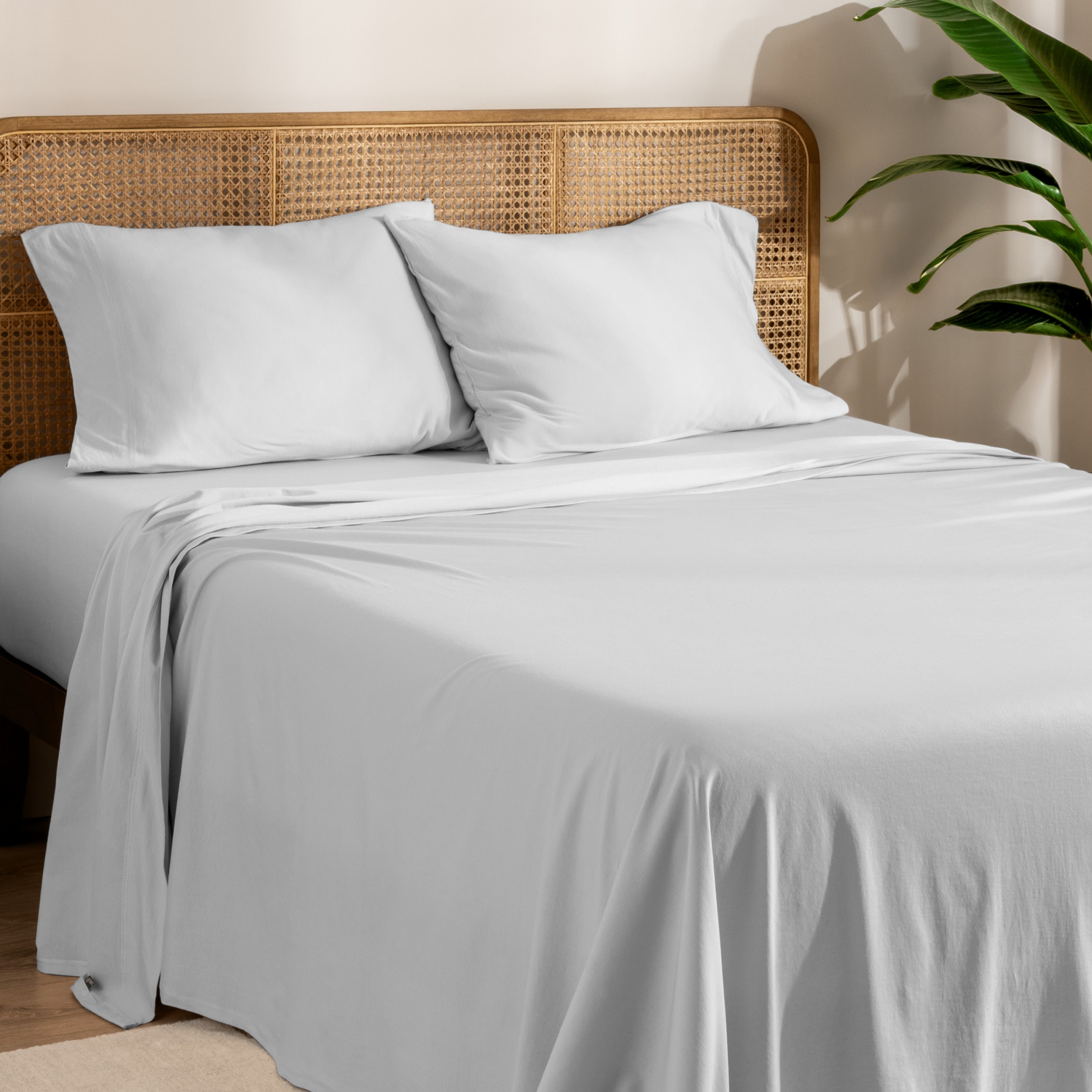 Organic jersey sheets and pillowcases on a bed with plants on the side in a bright and chill room scene.