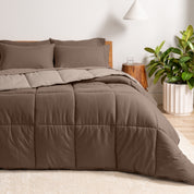A wooden bed frame with a reversible comforter and sheet set on the mattress in a bright warm room.