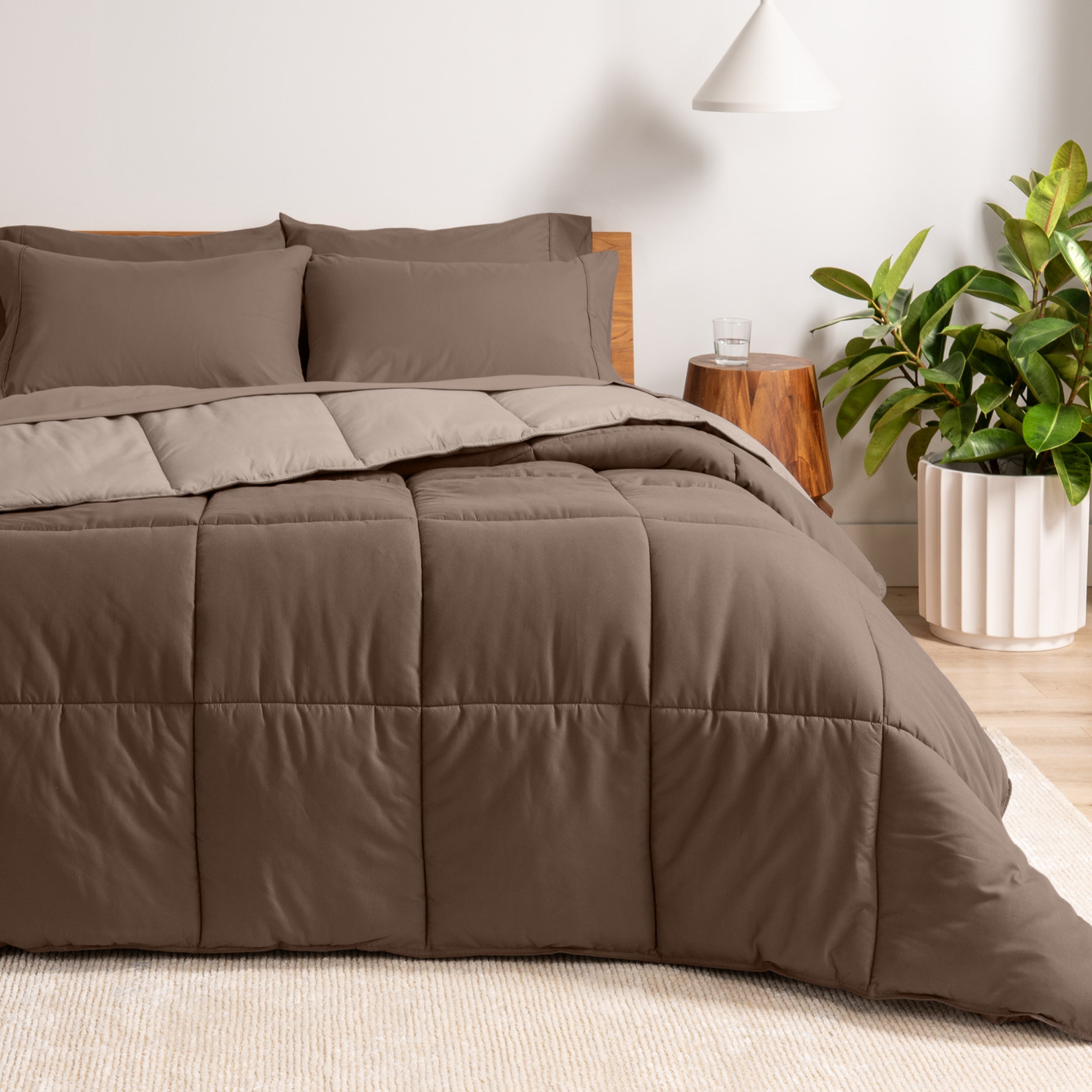 A wooden bed frame with a reversible comforter and sheet set on the mattress in a bright warm room.