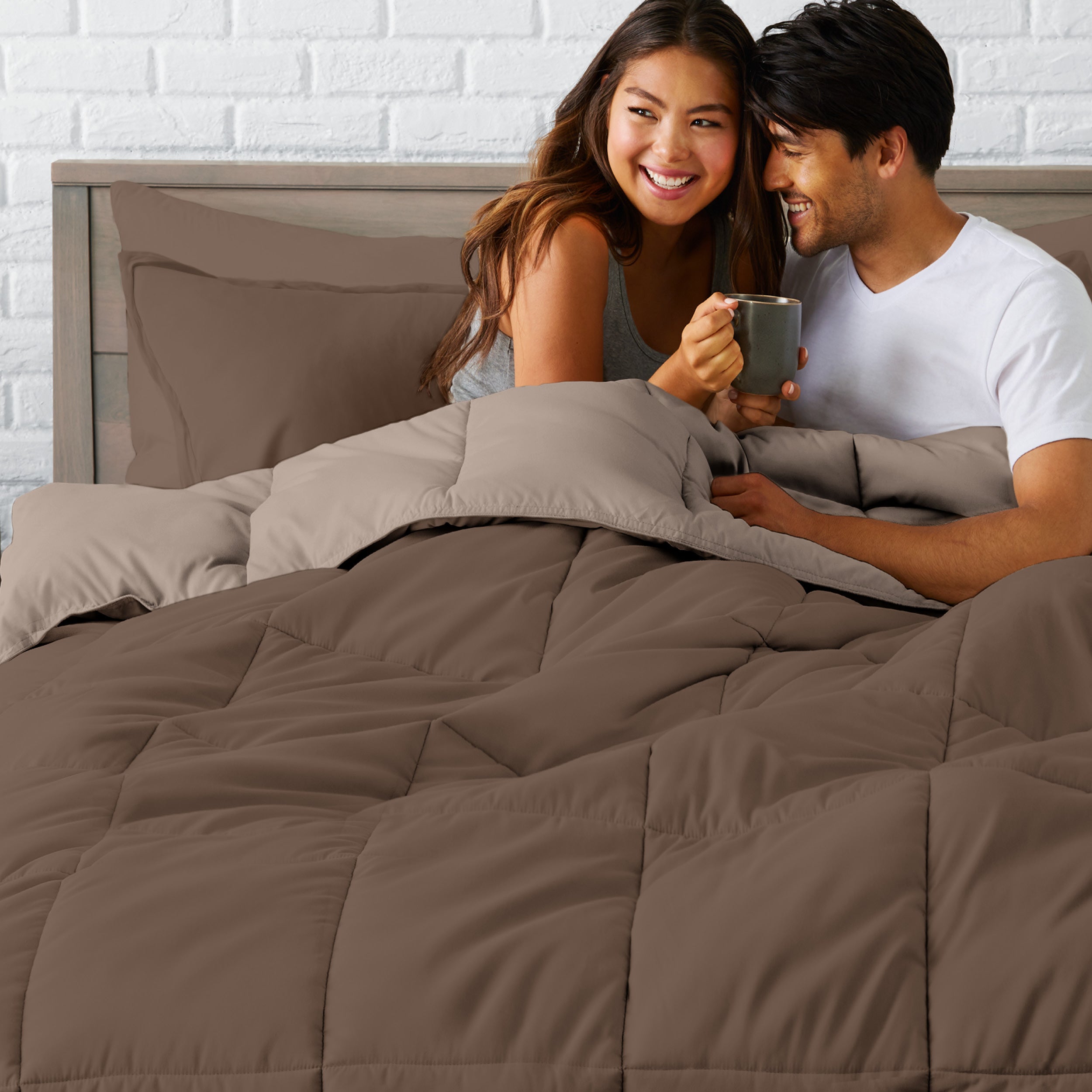 A couple sitting in a bed made with a reversible comforter and sheet set