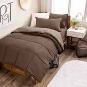 A wooden bed frame with a reversible comforter and sheet set on the mattress in a dorm style room.
