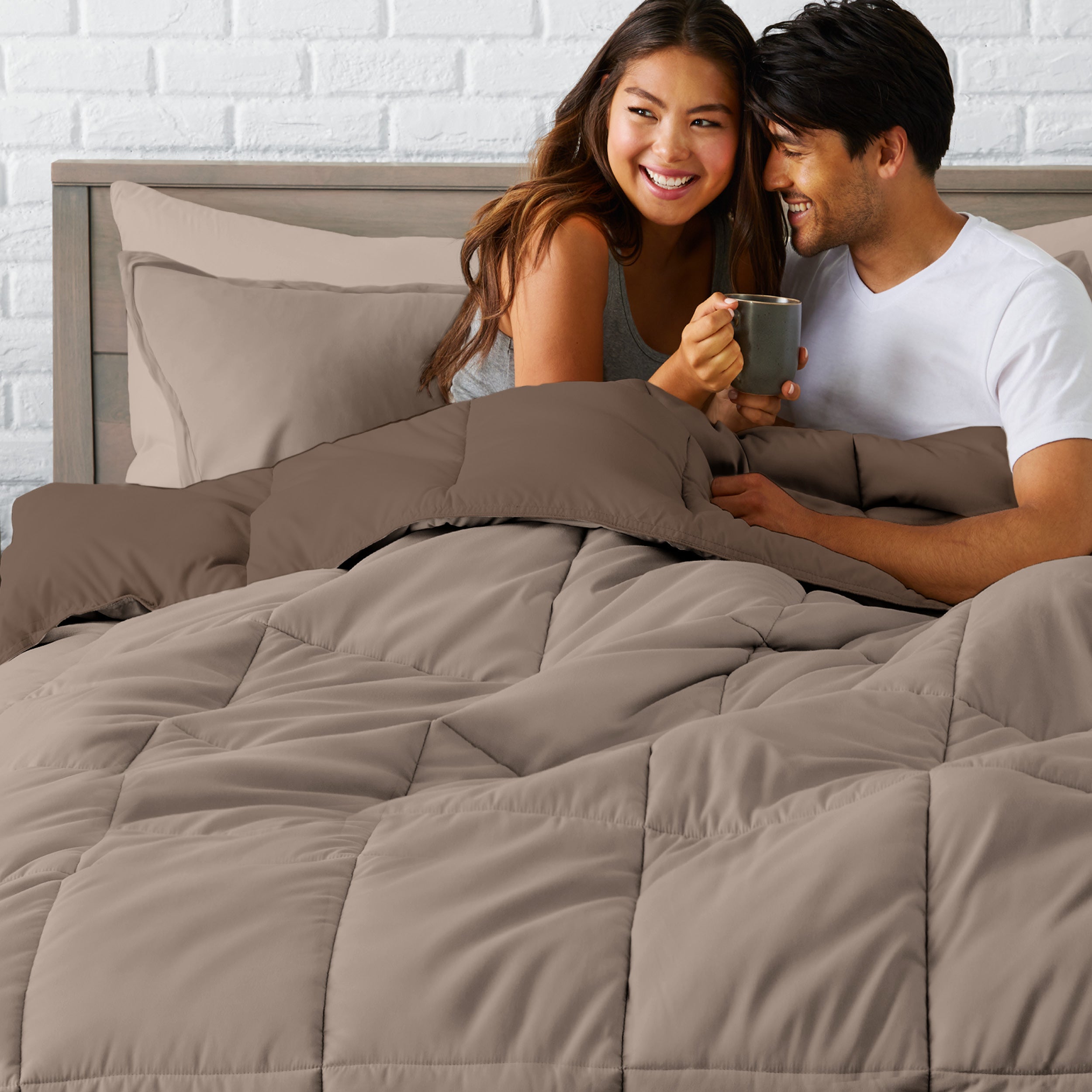 A couple sitting in a bed made with a reversible comforter and sheet set