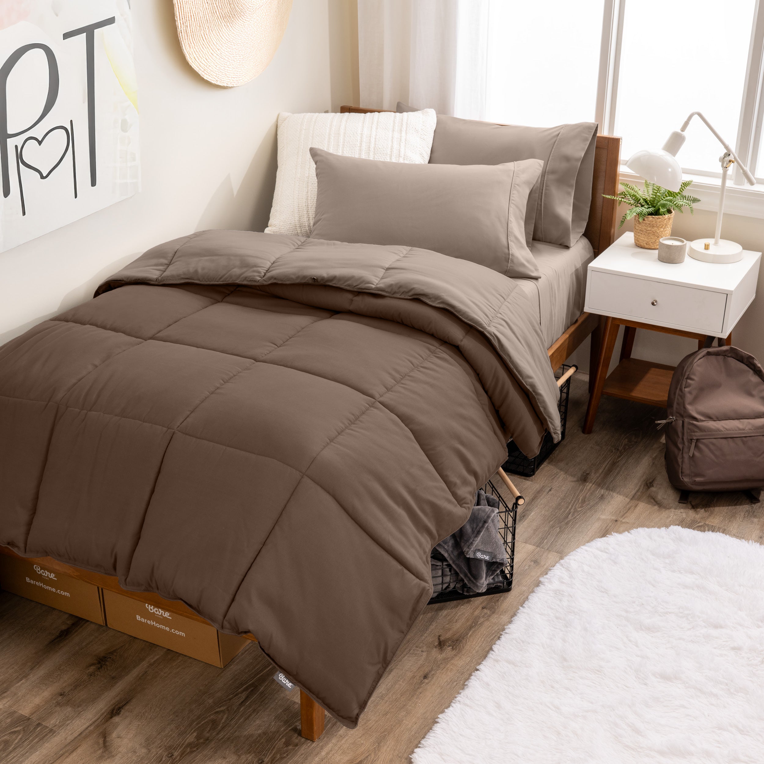 A wooden bed frame with a reversible comforter and sheet set on the mattress in a dorm style room.