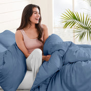 A woman sitting on a bed, wrapped in a comforter featuring the Bare Home flannel duvet set.