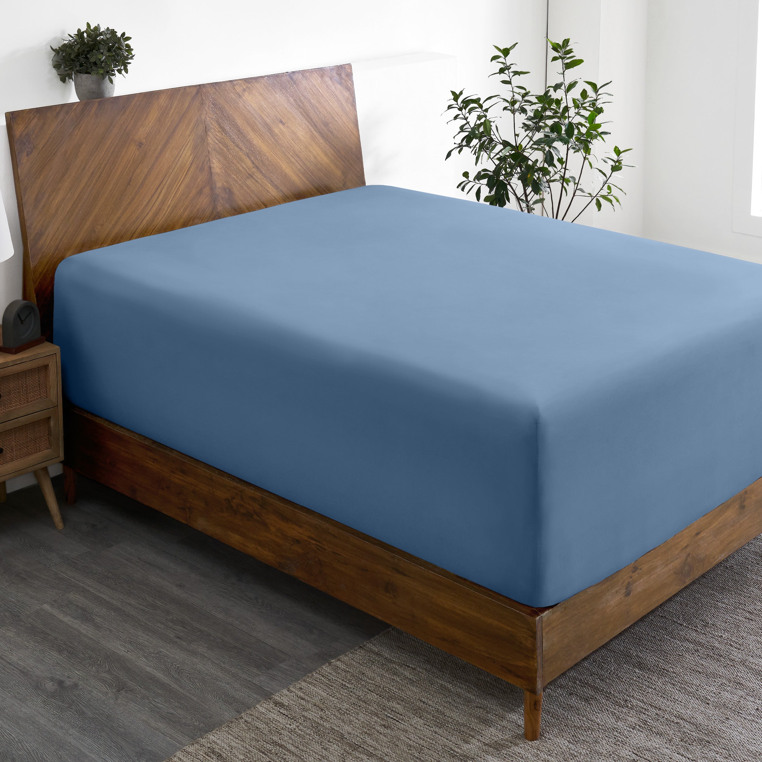 A wide corner view of a modern bed made with a microfiber fitted sheet on the mattress.