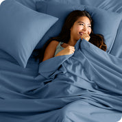 A smiling woman on a bed with a microfiber sheet over her
