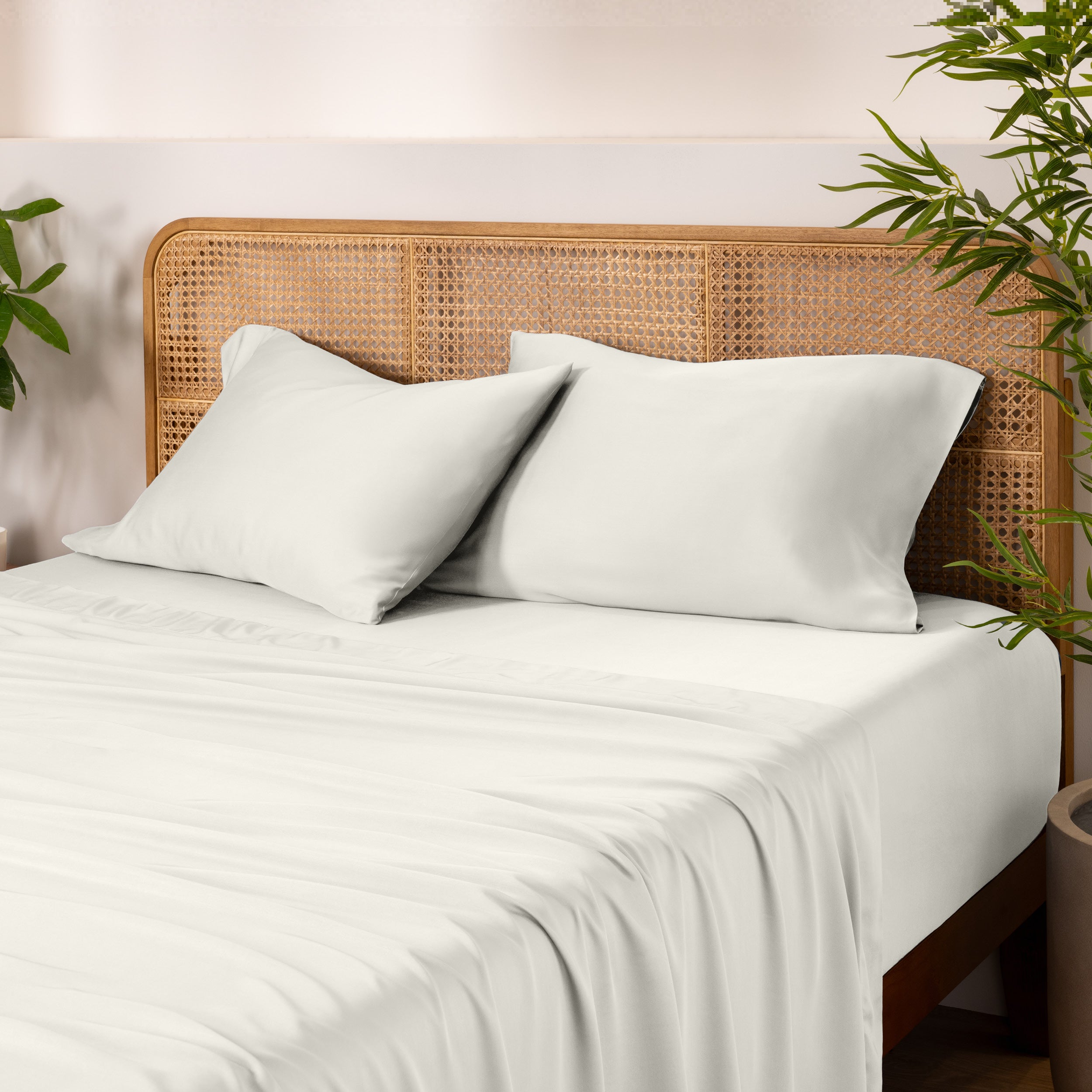 Bamboo bed sheets and pillowcases on a bed with a wicker headboard and plants in the background.