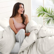 A woman sitting on a bed, wrapped in a comforter featuring the Bare Home flannel duvet set.