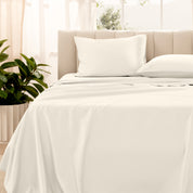 Organic sateen bedding on a bed with a beige headboard and plant in the corner.