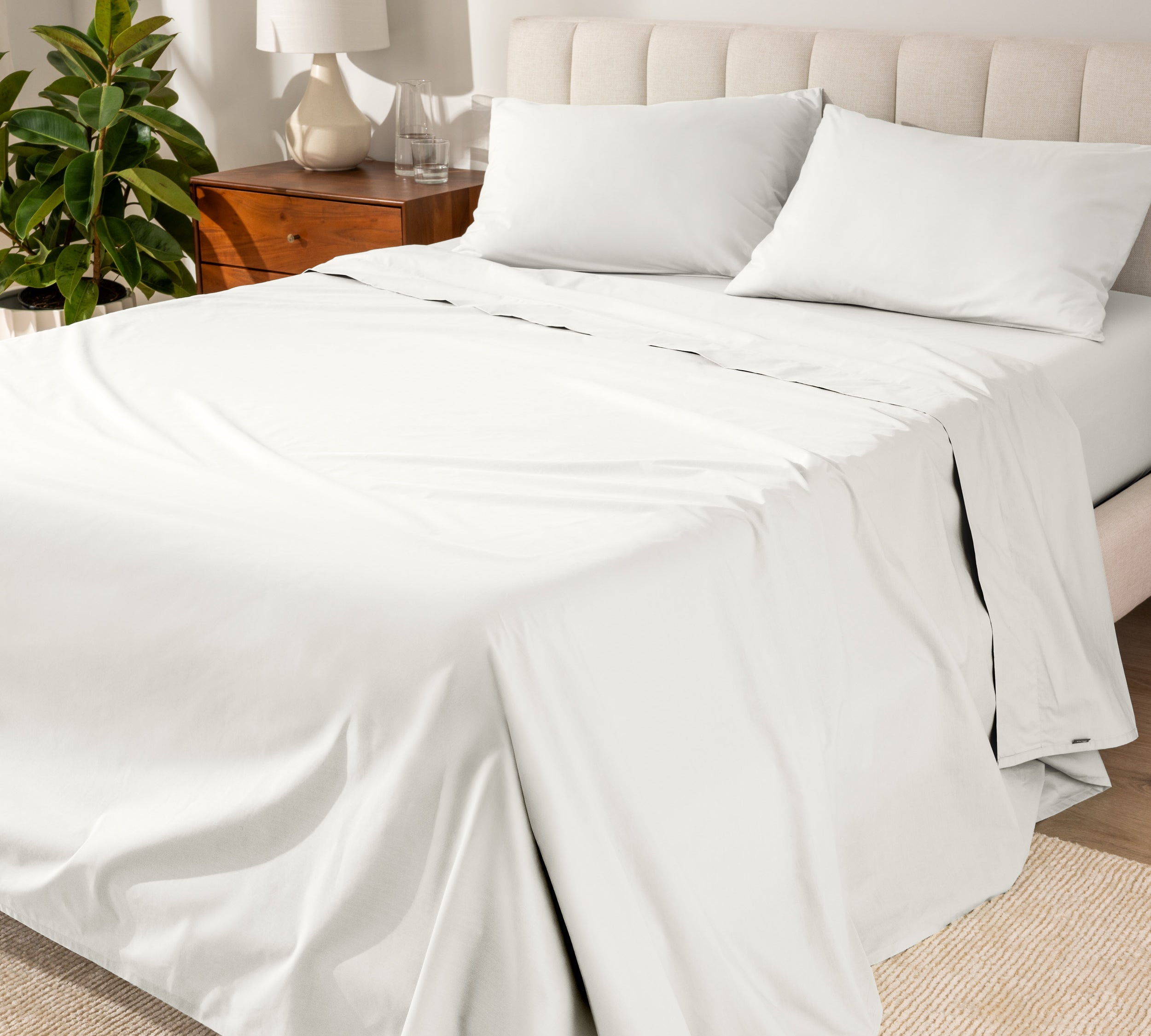 Organic cotton percale sheet set on a bed, with a flat sheet, fitted sheet, and two pillowcases displayed.