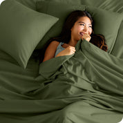 A smiling woman on a bed with a microfiber sheet over her