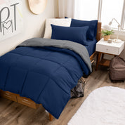 A wooden bed frame with a reversible comforter and sheet set on the mattress in a dorm style room.