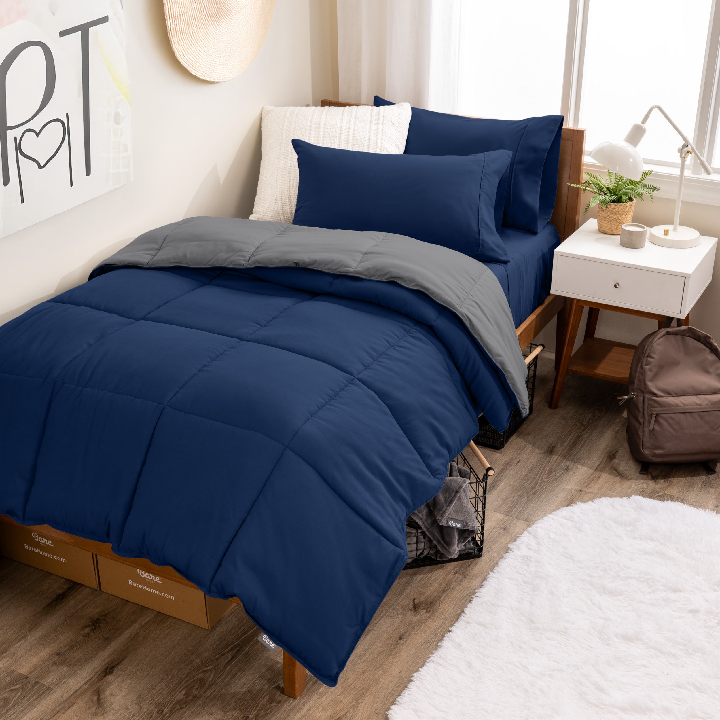A wooden bed frame with a reversible comforter and sheet set on the mattress in a dorm style room.