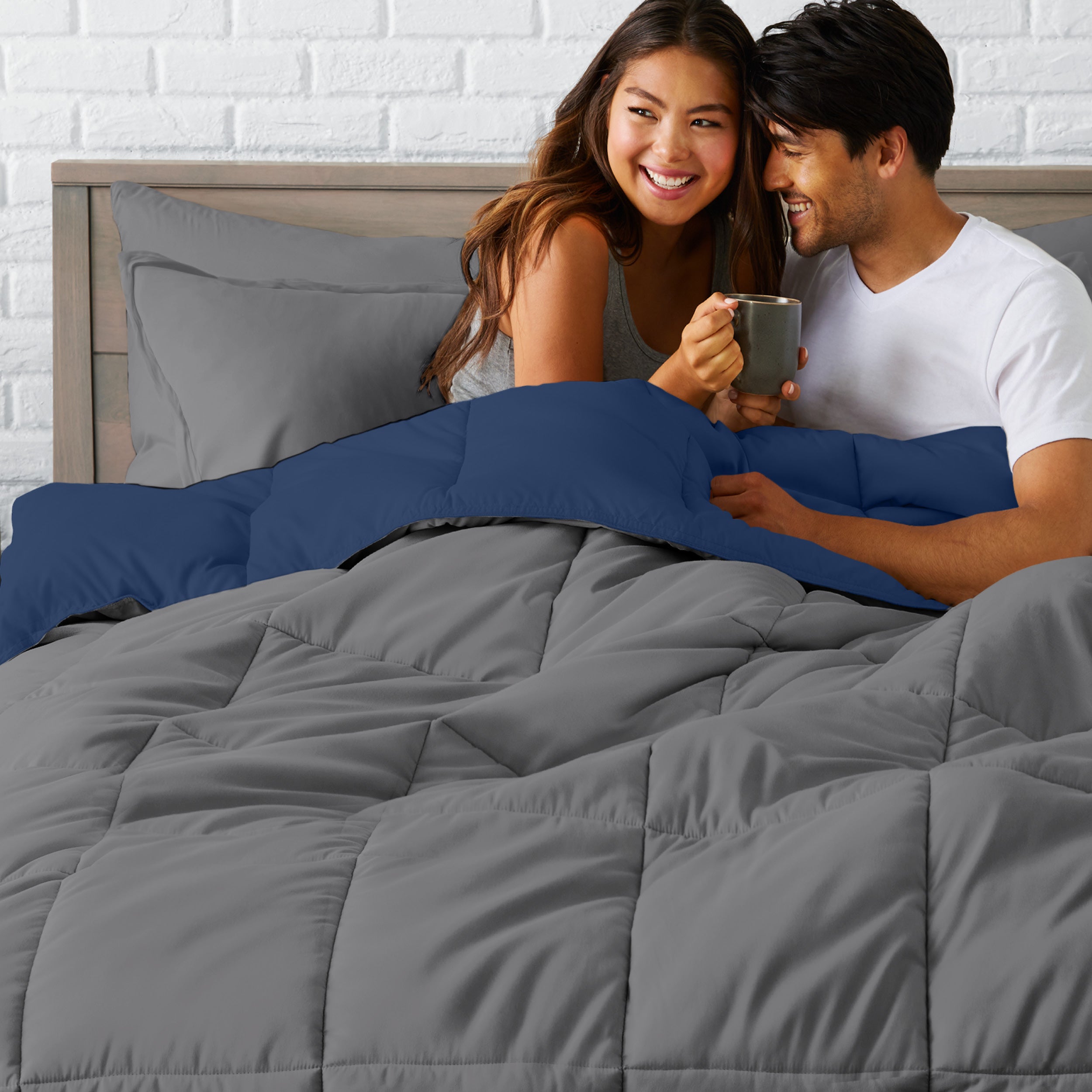 A couple sitting in a bed made with a reversible comforter and sheet set