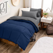 A wooden bed frame with a reversible comforter and sheet set on the mattress in a dorm style room.