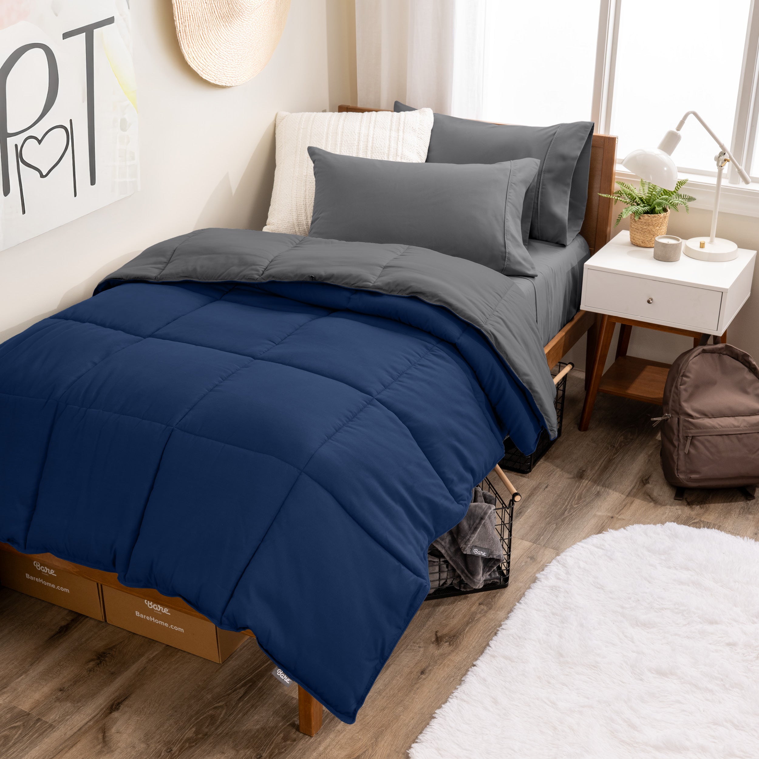 A wooden bed frame with a reversible comforter and sheet set on the mattress in a dorm style room.