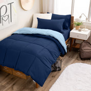A wooden bed frame with a reversible comforter and sheet set on the mattress in a dorm style room.