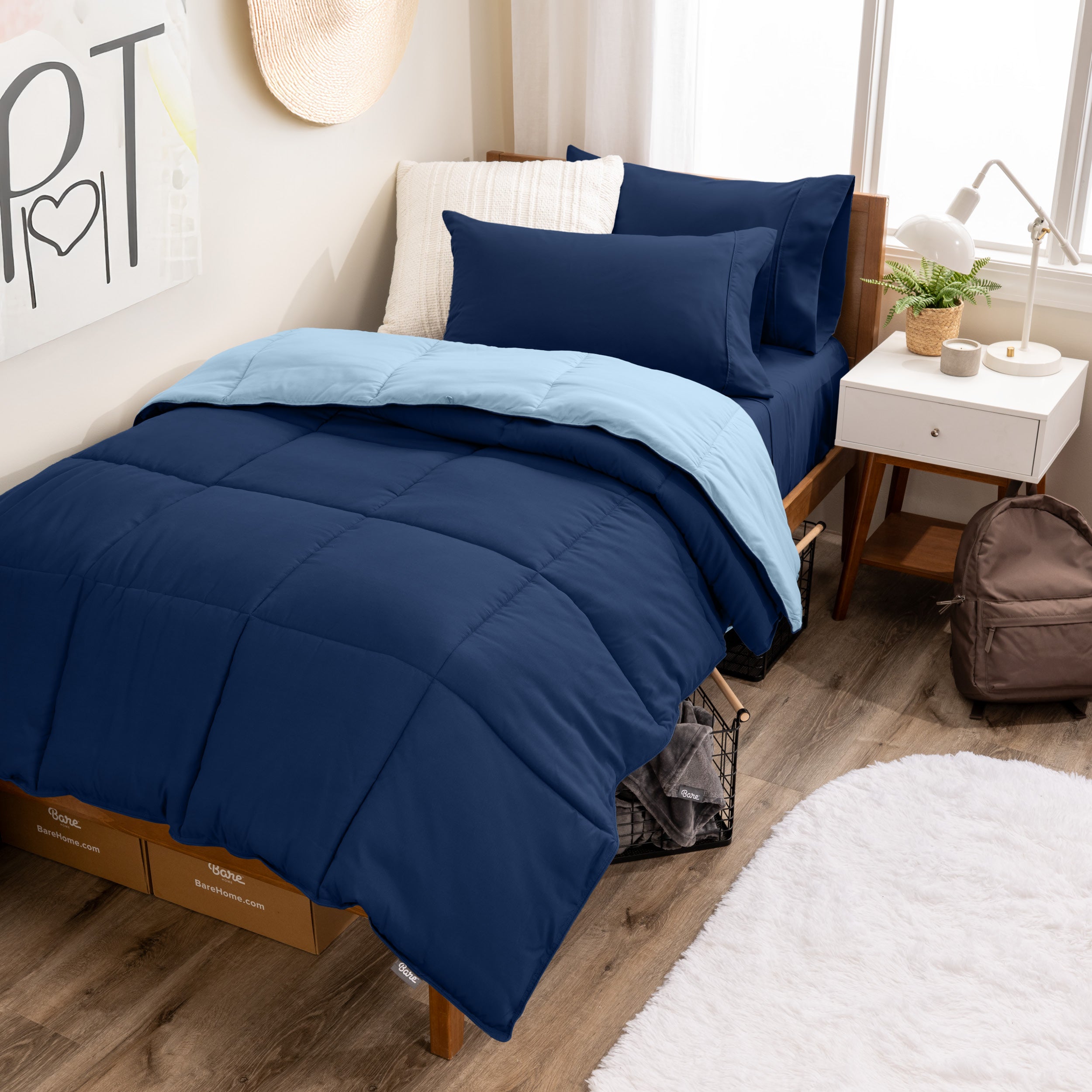 A wooden bed frame with a reversible comforter and sheet set on the mattress in a dorm style room.