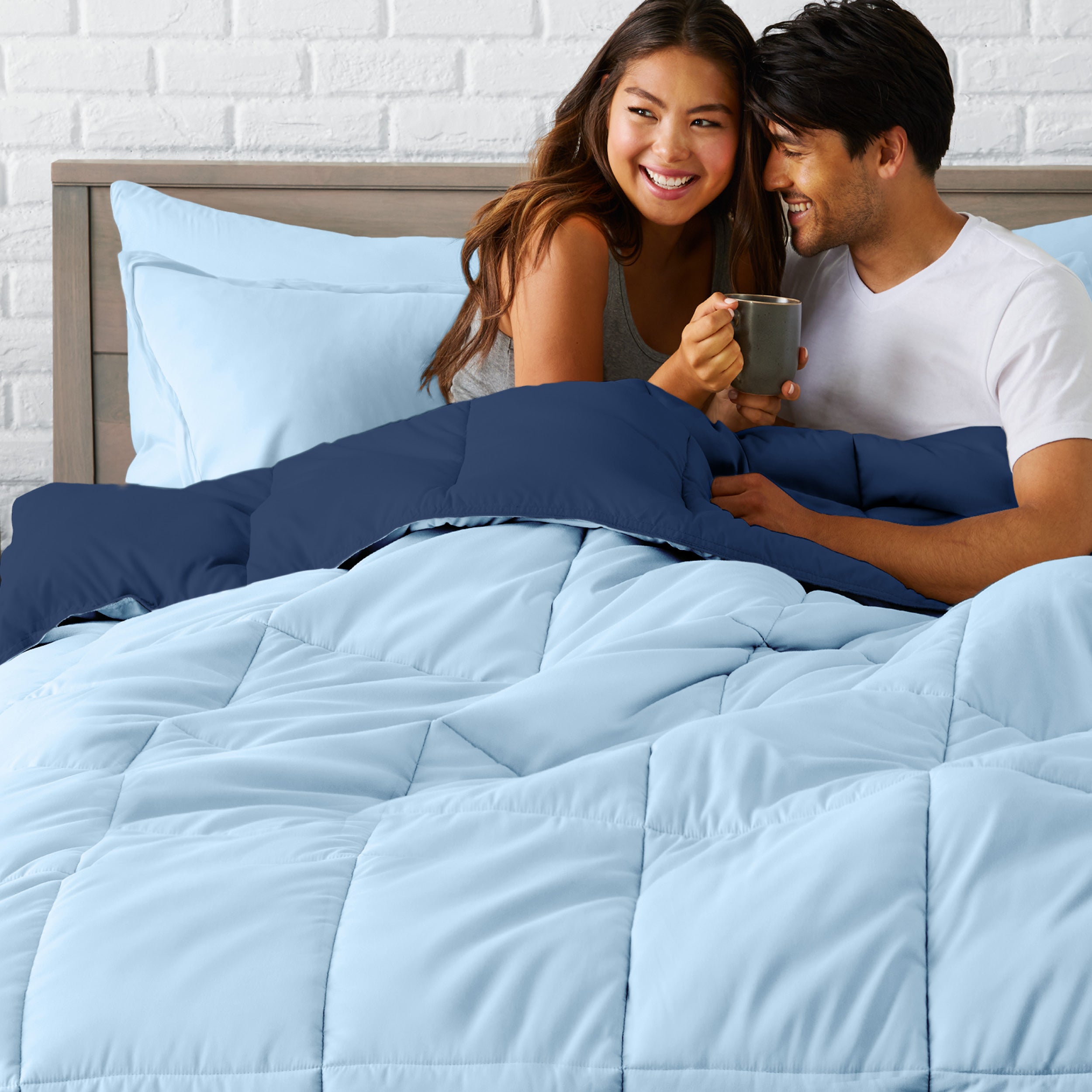 A couple sitting in a bed made with a reversible comforter and sheet set