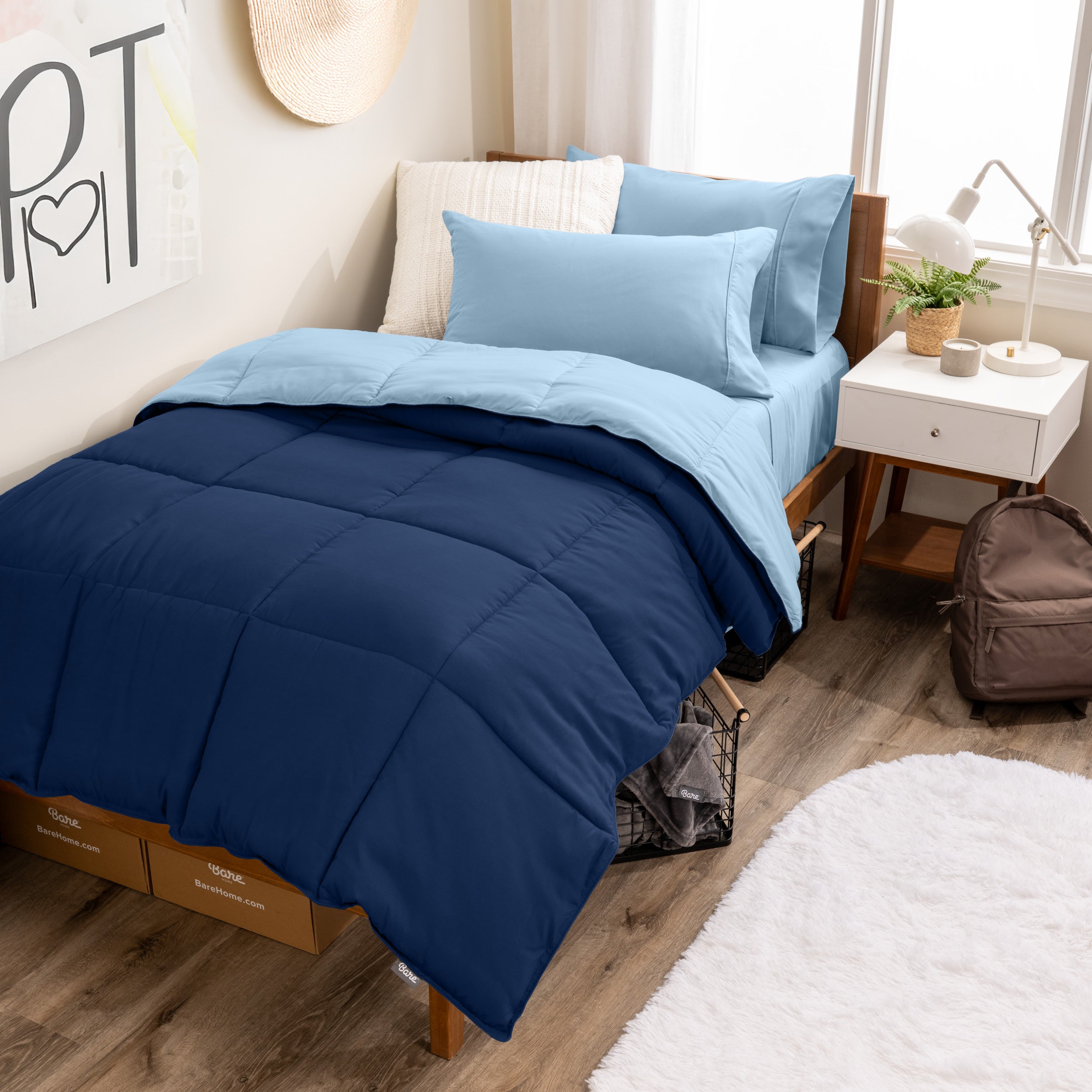 A wooden bed frame with a reversible comforter and sheet set on the mattress in a dorm style room.