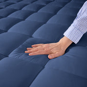 A hand is feeling the soft cotton texture of the mattress pad.