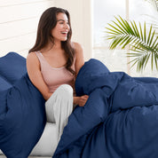 A woman sitting on a bed, wrapped in a comforter featuring the Bare Home flannel duvet set.