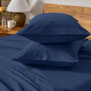 Two pillows with flannel pillowcases stacked on a bed with a wooden headboard and side table in the background.