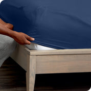 A man is kneeling while putting a fitted sheet on a mattress
