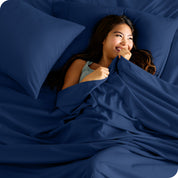 A smiling woman on a bed with a microfiber sheet over her