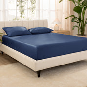Organic cotton fitted sheet on a bed in a bedroom with a plant and window in the background