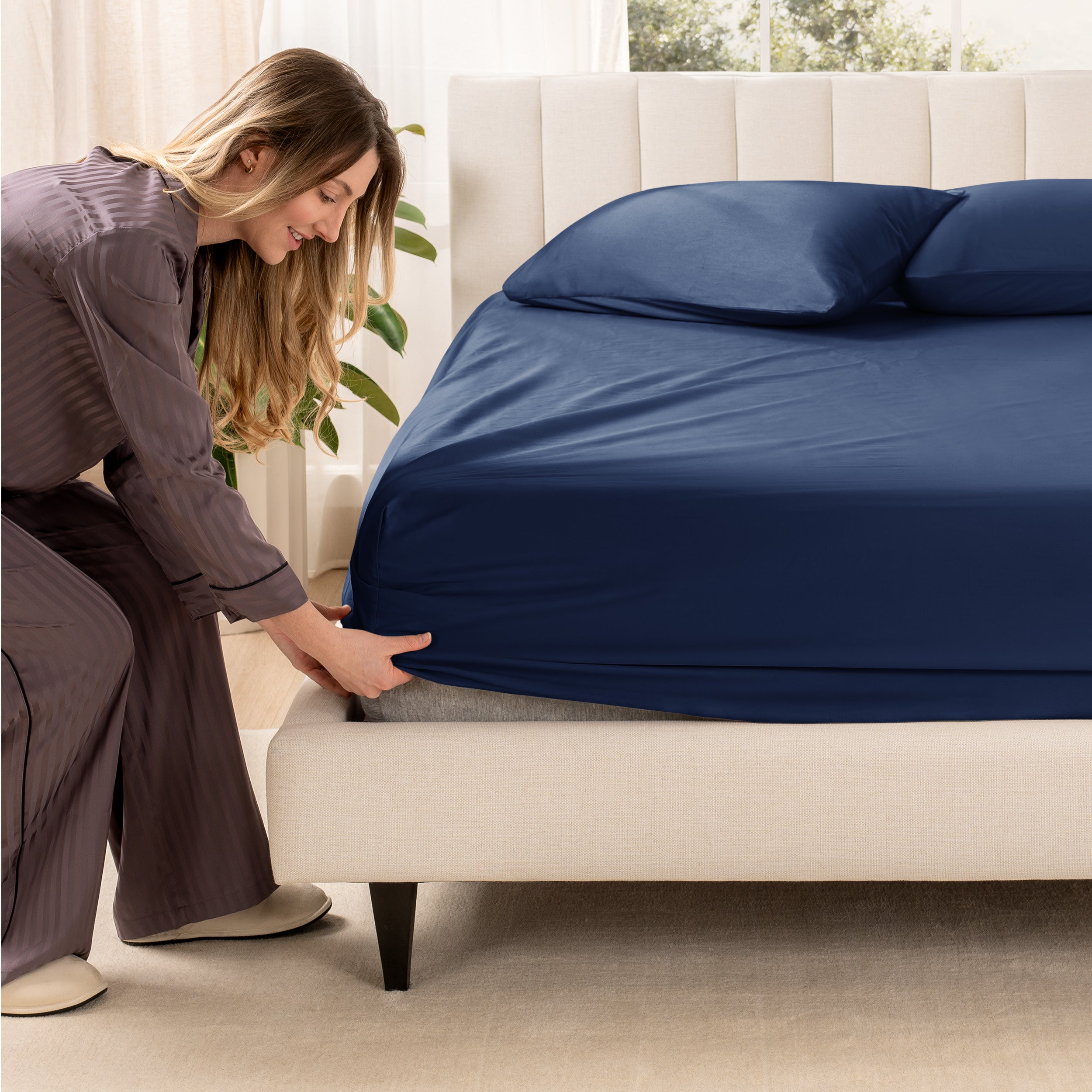 A woman is putting a fitted sheet on a mattress