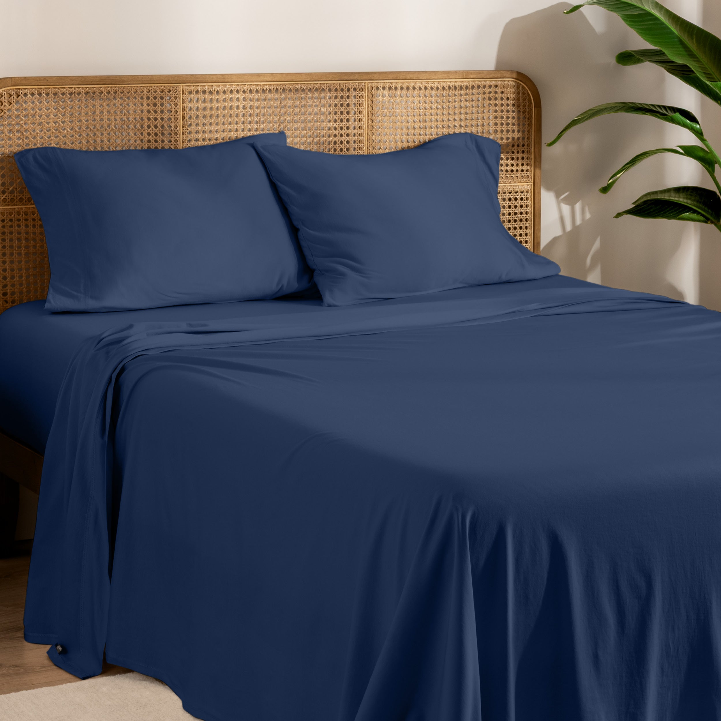 Organic jersey sheets and pillowcases on a bed with plants on the side in a bright and chill room scene.