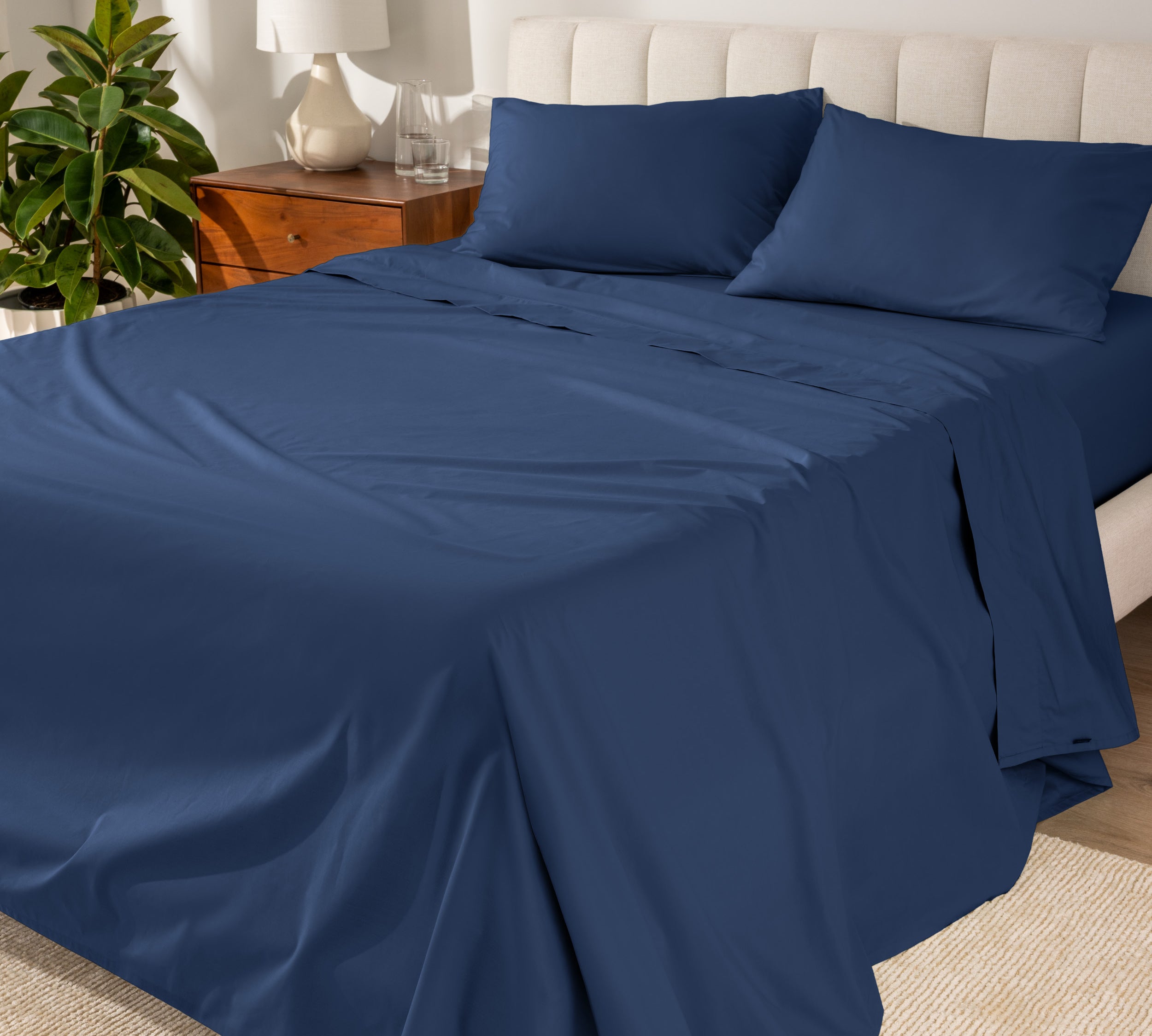 Organic cotton percale sheet set on a bed, with a flat sheet, fitted sheet, and two pillowcases displayed.