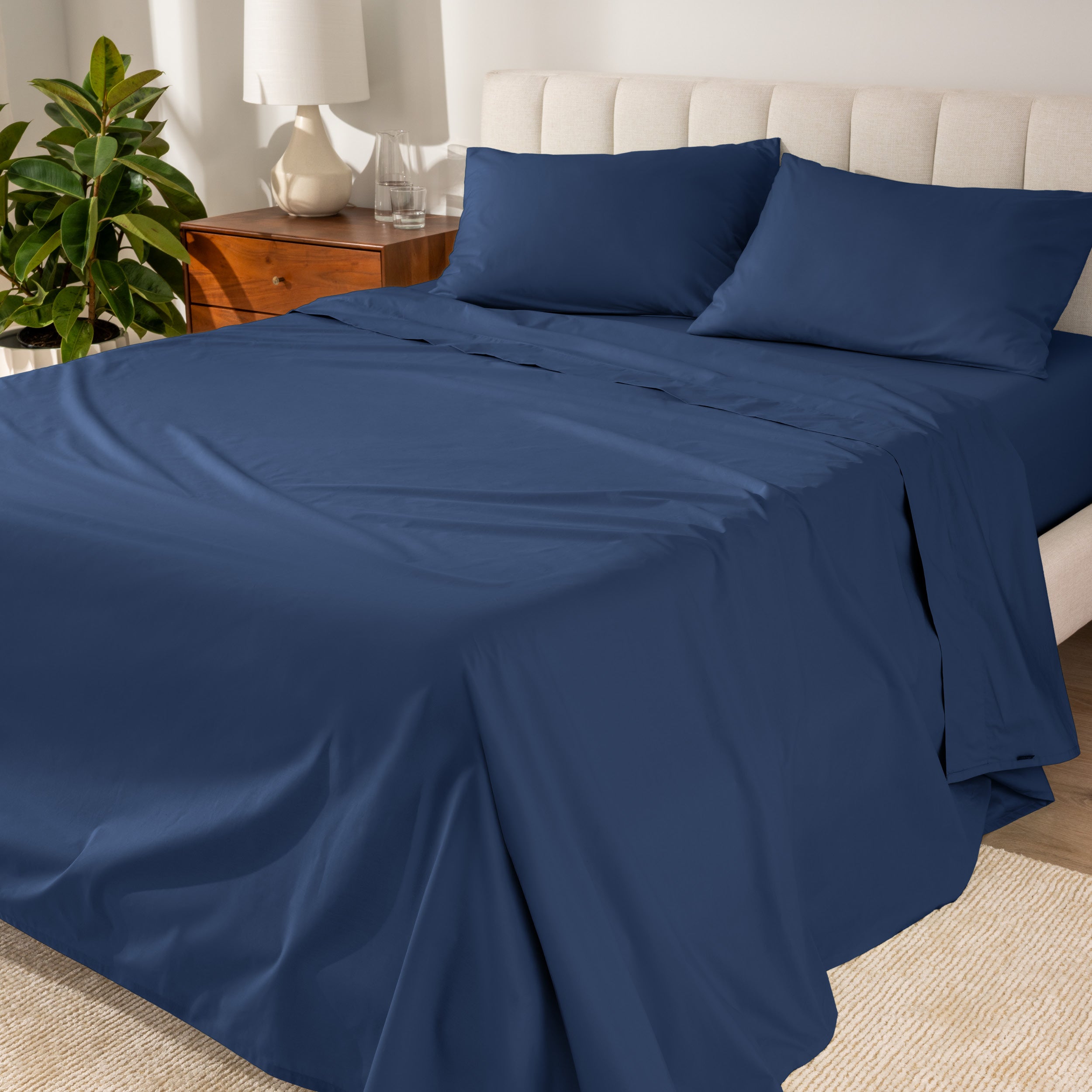 Organic cotton percale sheet set on a bed, with a flat sheet, fitted sheet, and two pillowcases displayed.