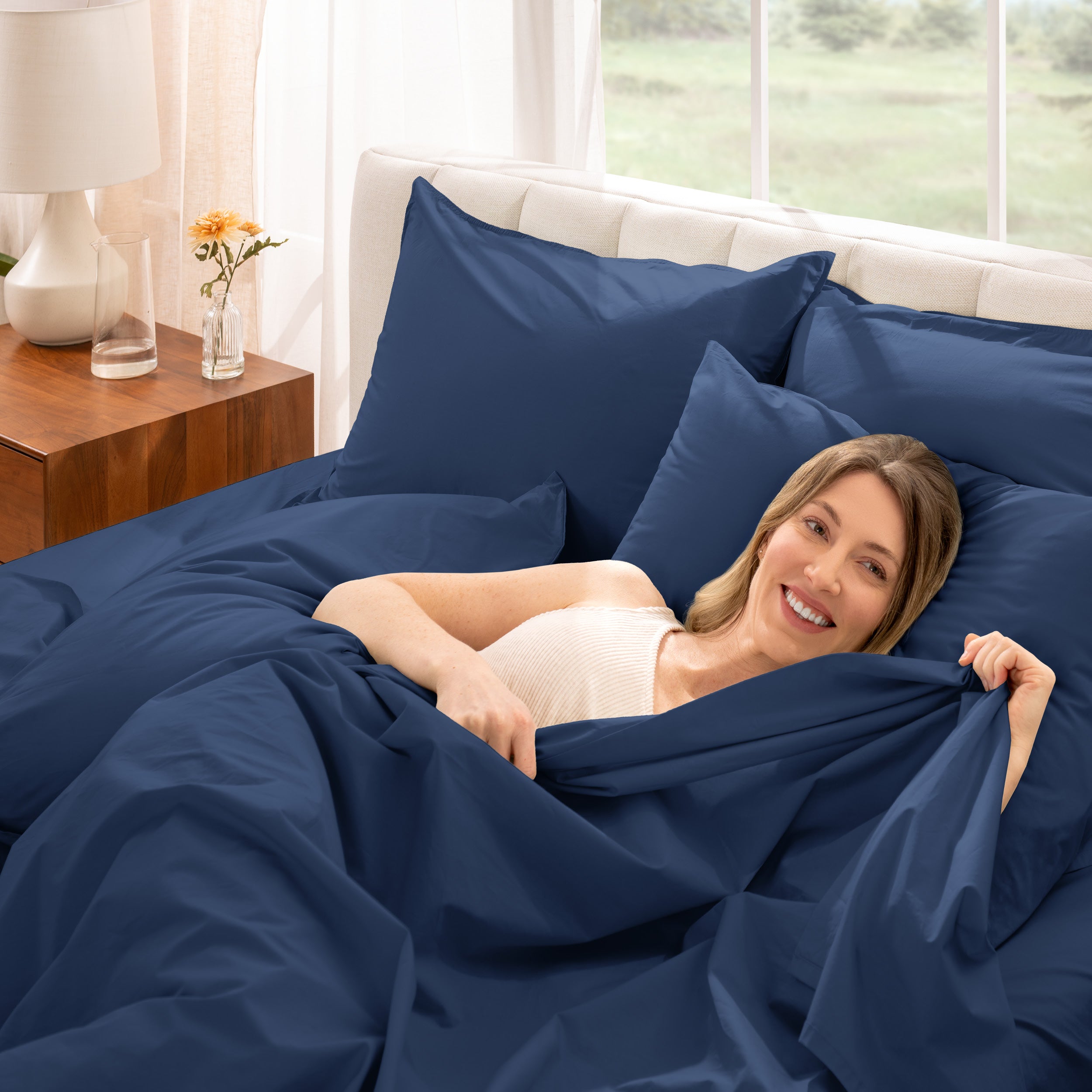 Woman lying in bed under percale sheets with a bright room setting