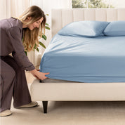 A woman is putting a fitted sheet on a mattress