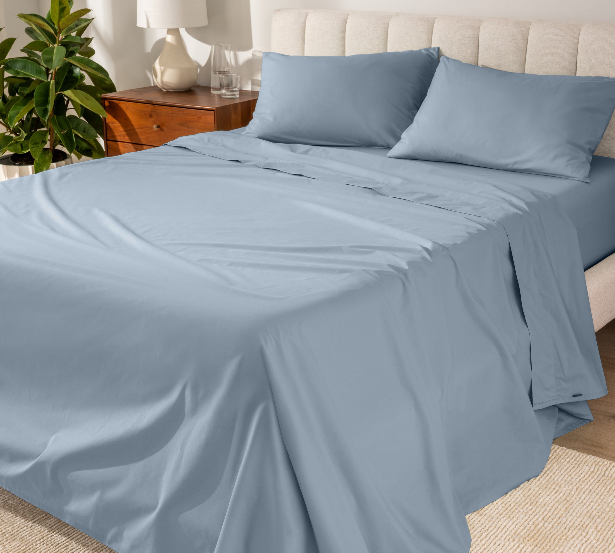 Organic cotton percale sheet set on a bed, with a flat sheet, fitted sheet, and two pillowcases displayed.