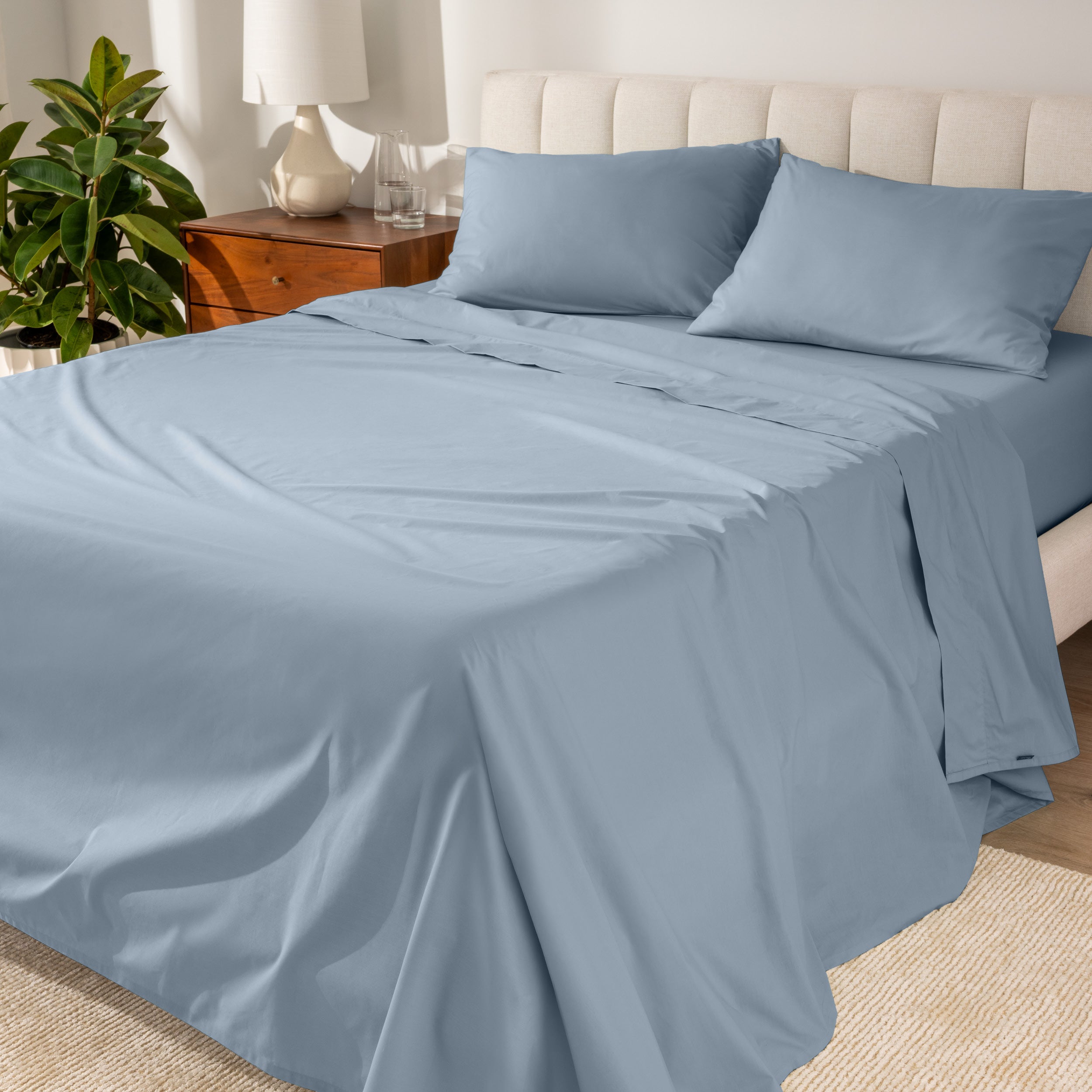 Organic cotton percale sheet set on a bed, with a flat sheet, fitted sheet, and two pillowcases displayed.